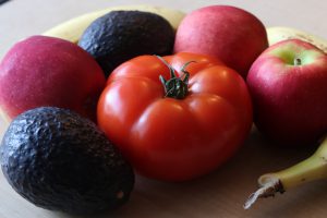 A tomato, two avocados, three apples and two bananas sit on a table.