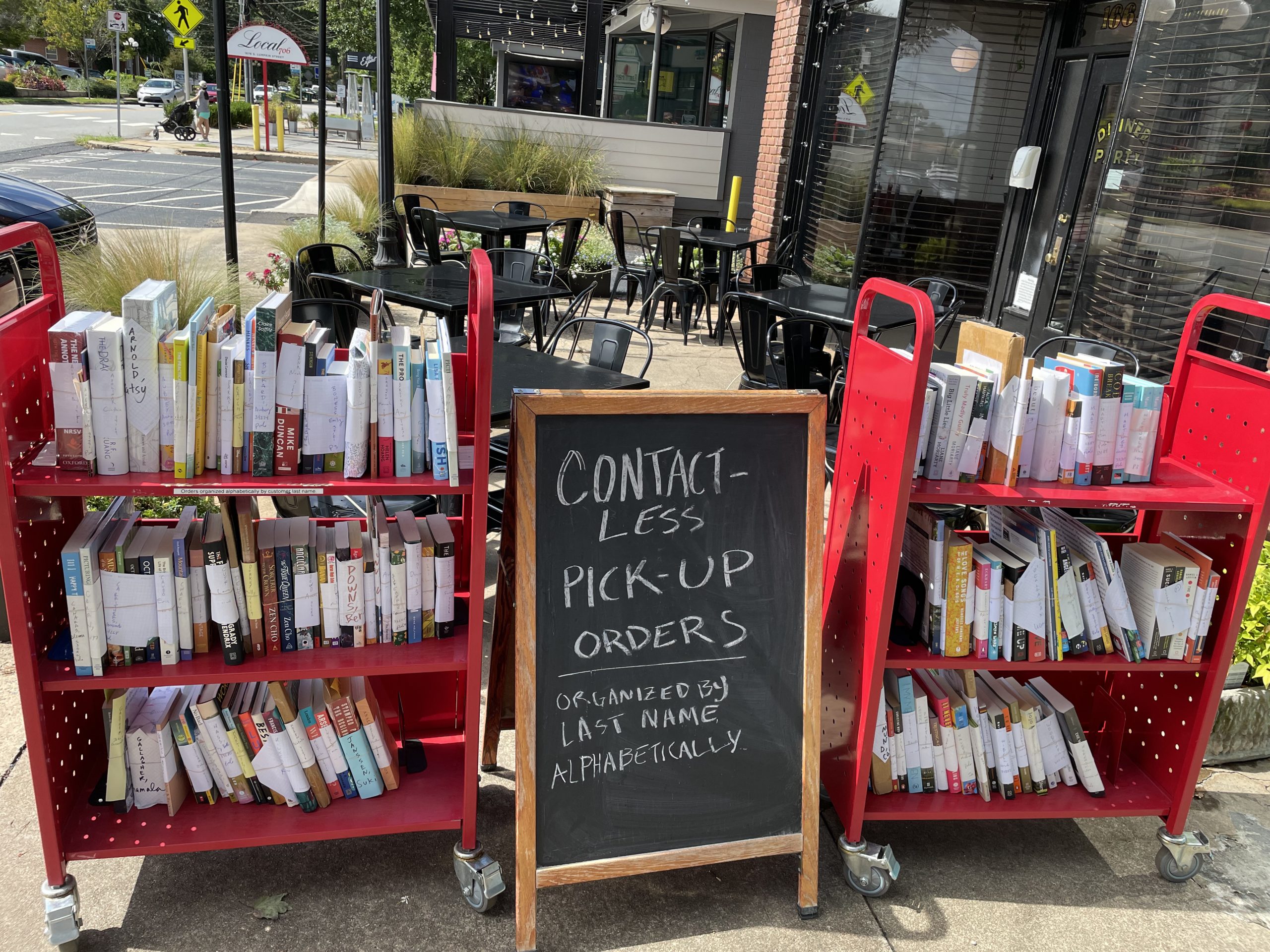 Two red carts loaded with books sit behind a chalkboard sign.