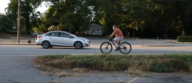 man rides bike on road with car in background