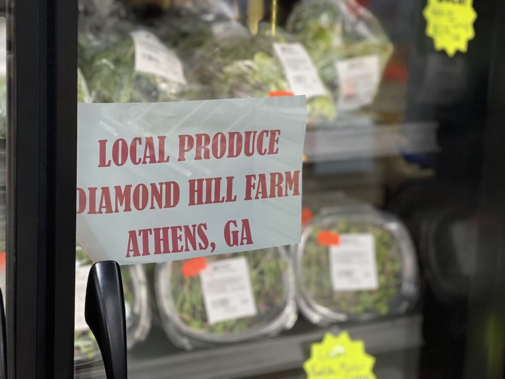 A paper sign featuring a charming red serif font advertises a vibrant selection of lettuces, micro-greens, and radish greens from Athens-based Diamond Hill Farm.