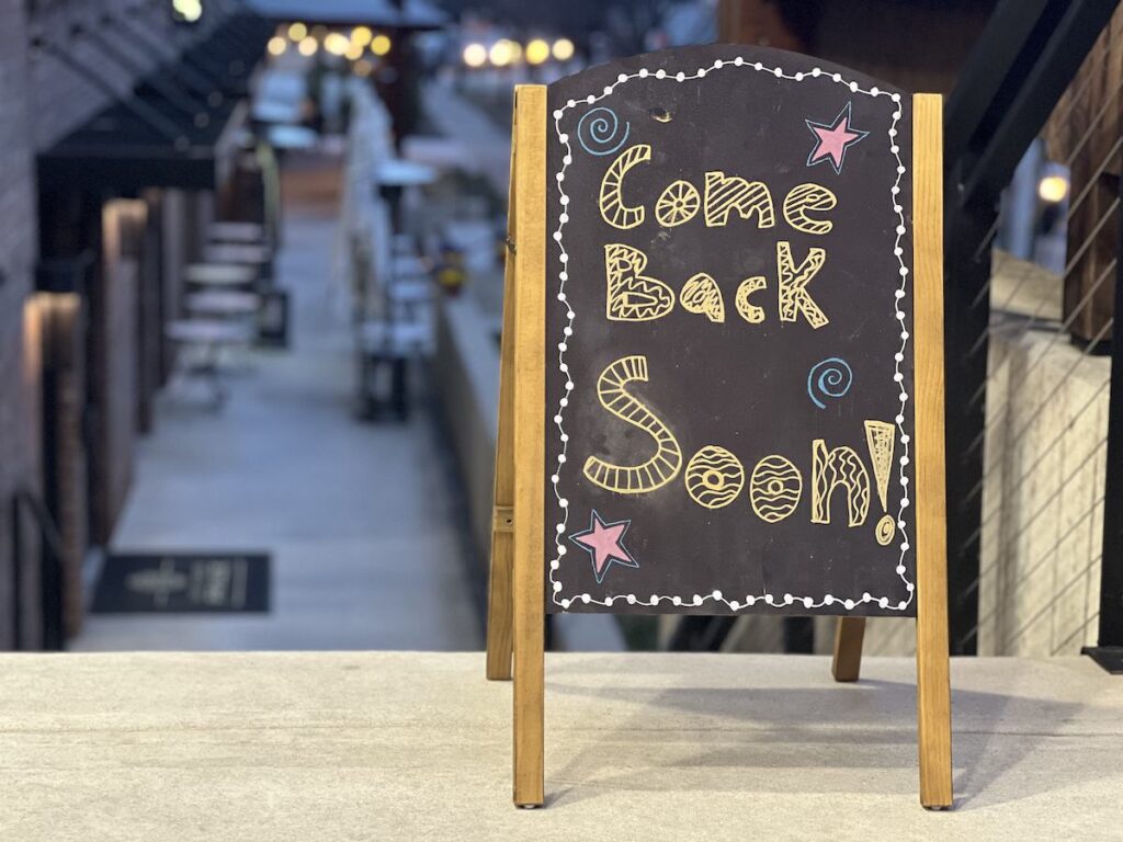 A decorative A-fold chalkboard sign outside Prince Market's patio entrance bids customers goodbye, featuring charming handcrafted designs.
