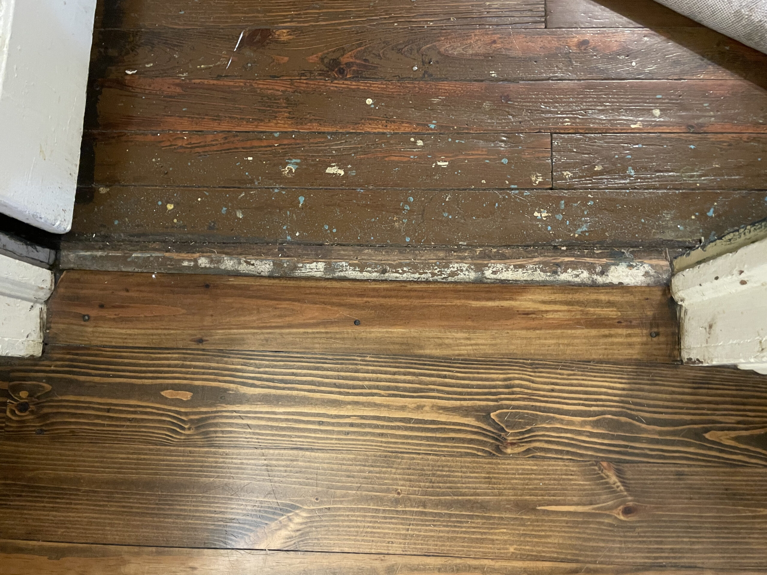 Original dark pine floorboards pictured next to newer floorboards on the floor of a house.