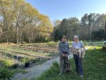 A man and a woman stand with two dogs in front of community food plots.