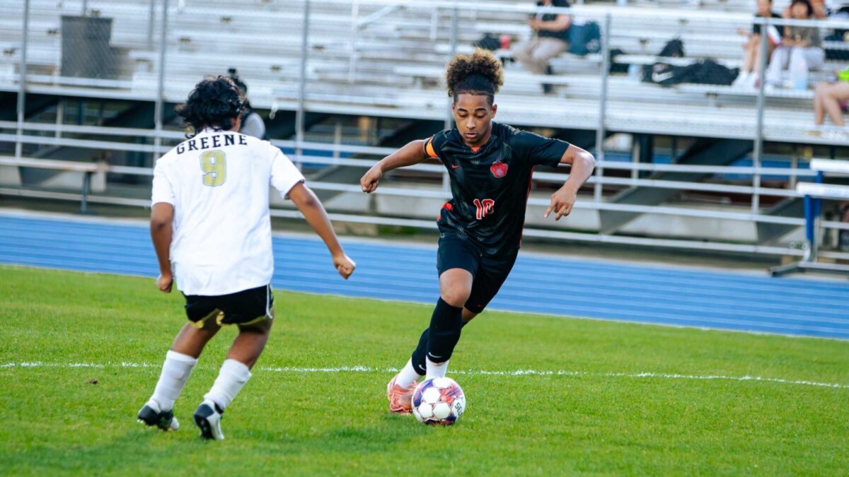 A soccer player dribbles against an opponent