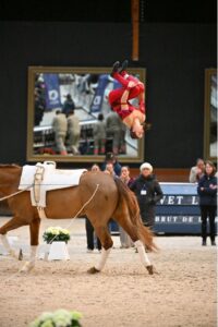 An equestrian performs a backflip while riding a horse.