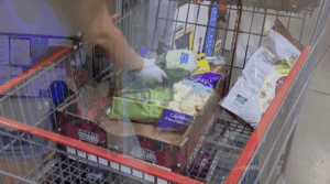 Hand in grocery basket among an assortment of groceries