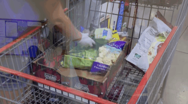 Hand in grocery basket among an assortment of groceries