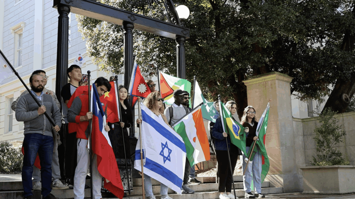 Group of students holding flags in front of the UGA arch