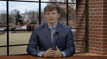 A sports anchor sits at a desk in the newsroom