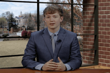 A sports anchor sits at a desk in the newsroom