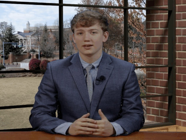 A sports anchor sits at a desk in the newsroom