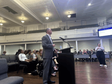 Man speaking at podium with microphone at board of education meeting