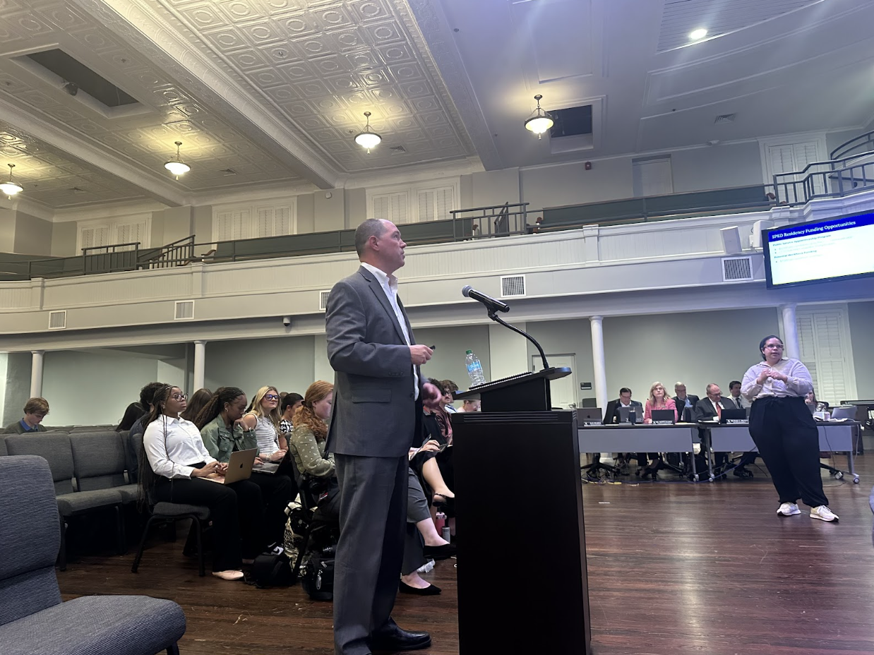 Man speaking at podium with microphone at board of education meeting