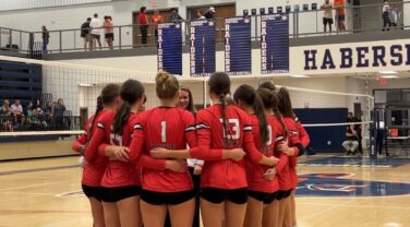 A group of volleyball players huddles before a match.