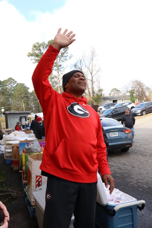 A man waves and smiles outside in a parking lot