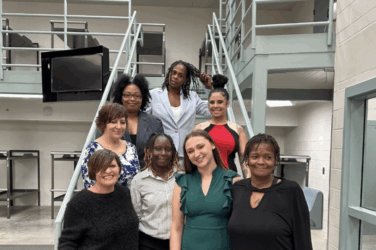 A group of women stands on the stairs and smiles at the camera from within the jail.