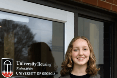 Woman stands in front of a glass door smiling on the University of Georgia campus