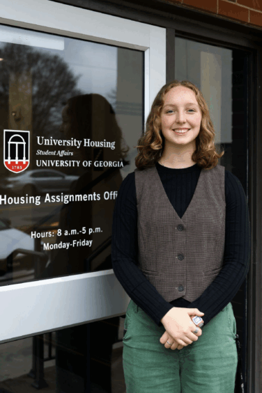 Woman stands in front of a glass door smiling on the University of Georgia campus