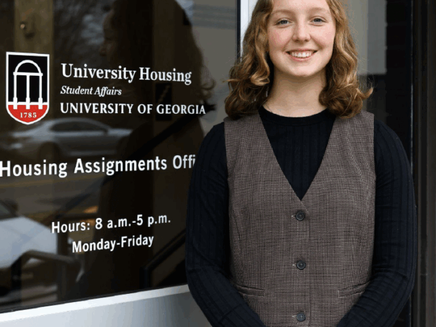 Woman stands in front of a glass door smiling on the University of Georgia campus