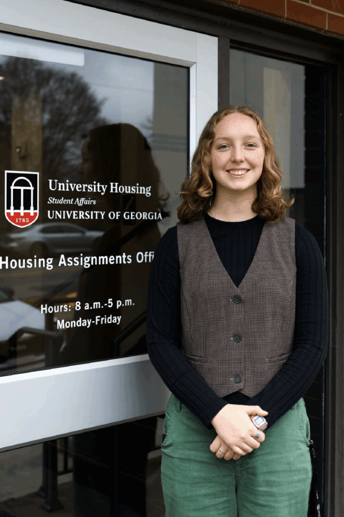Woman stands in front of a glass door smiling on the University of Georgia campus