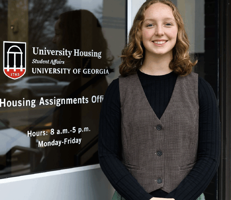 Woman stands in front of a glass door smiling on the University of Georgia campus
