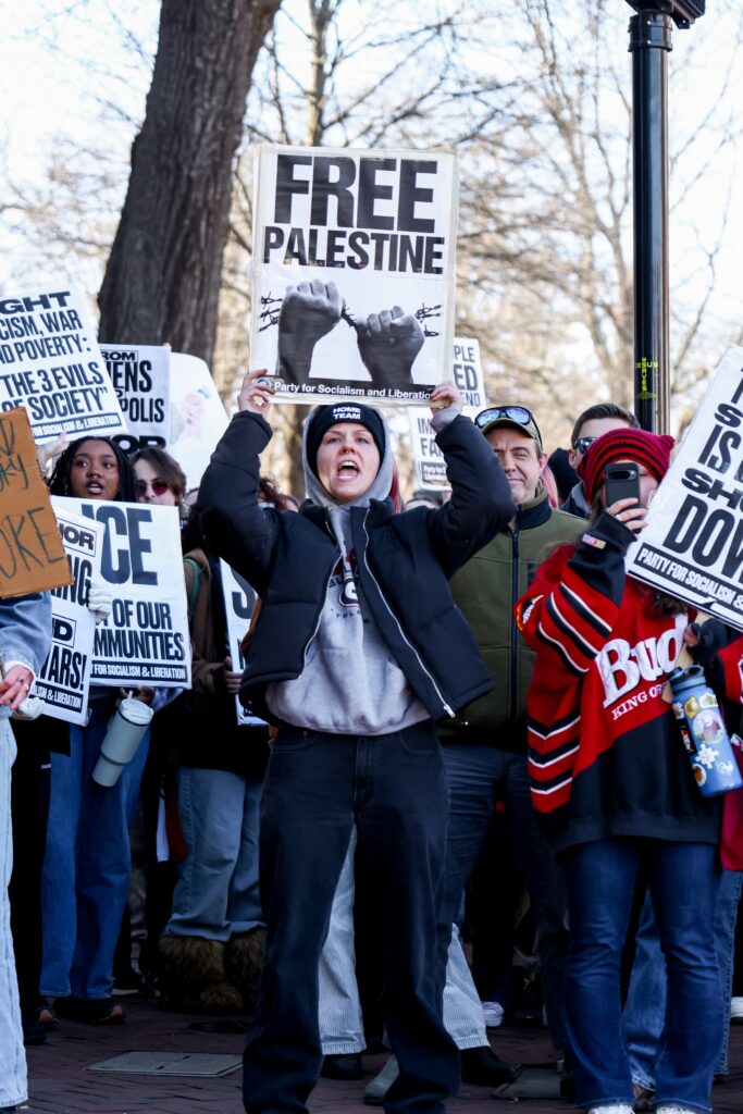 A woman chants loudly while holding a Free Palestine sign in a group of protestors.