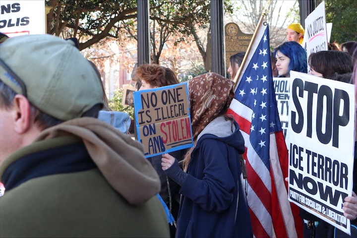 A woman carries a sign and a flag among other people during a protest.