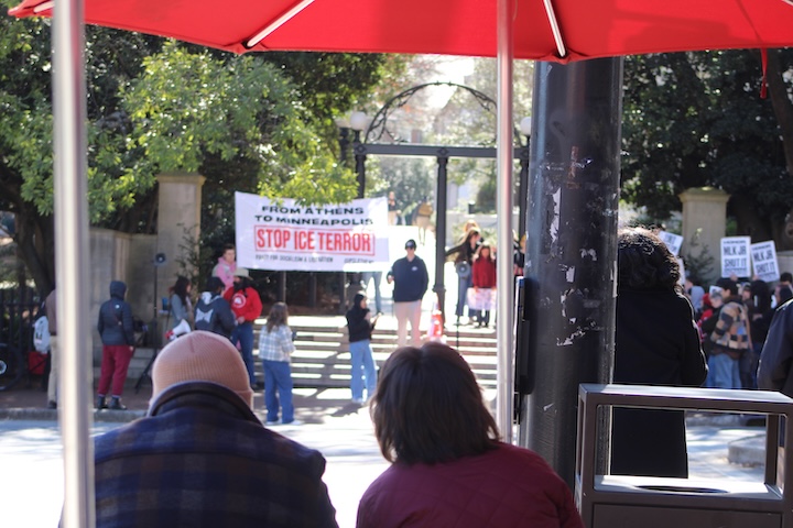 Stop ICE Terror sign is held near the University of Georgia arch among a group of protestors while others watch.