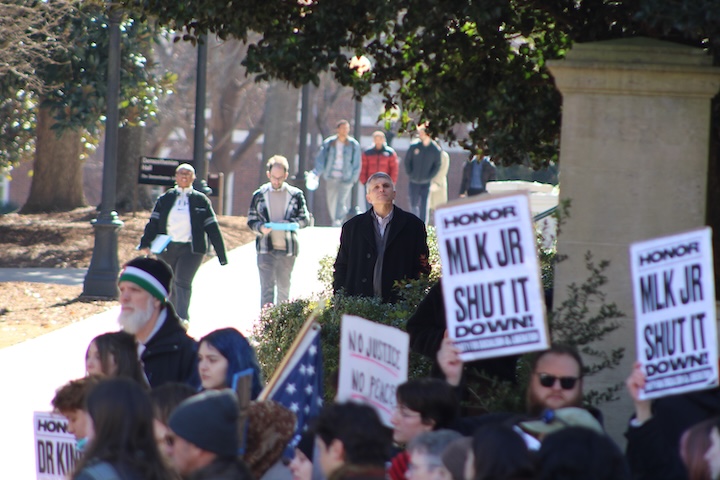 A group of people hold signs while others walk past during a protest.