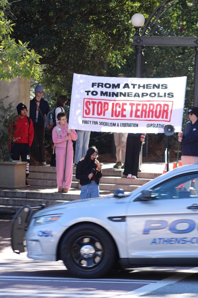 Woman looks at her phone while in front of a group of people holding a sign as a police car drives by