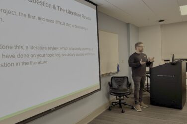 Man stands at the front of classroom with words projected on a screen