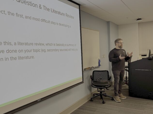 Man stands at the front of classroom with words projected on a screen
