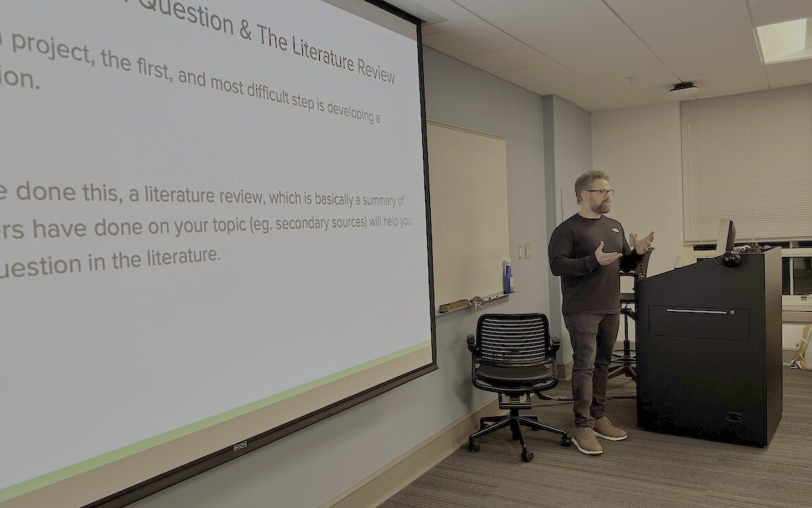 Man stands at the front of classroom with words projected on a screen