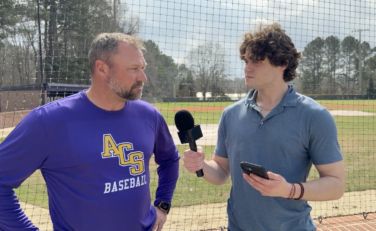 a sports journalist interviews a baseball coach on the field