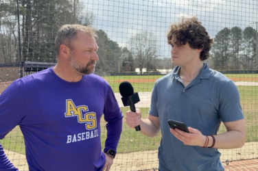 a sports journalist interviews a baseball coach on the field