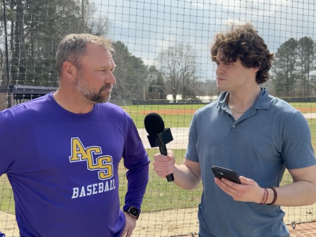 a sports journalist interviews a baseball coach on the field