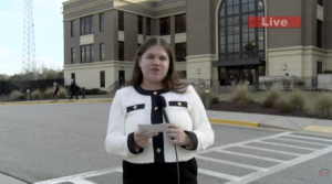 A reporter stands outside a courthouse with a microphone