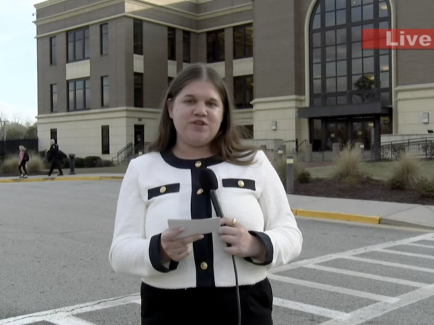 A reporter stands outside a courthouse with a microphone