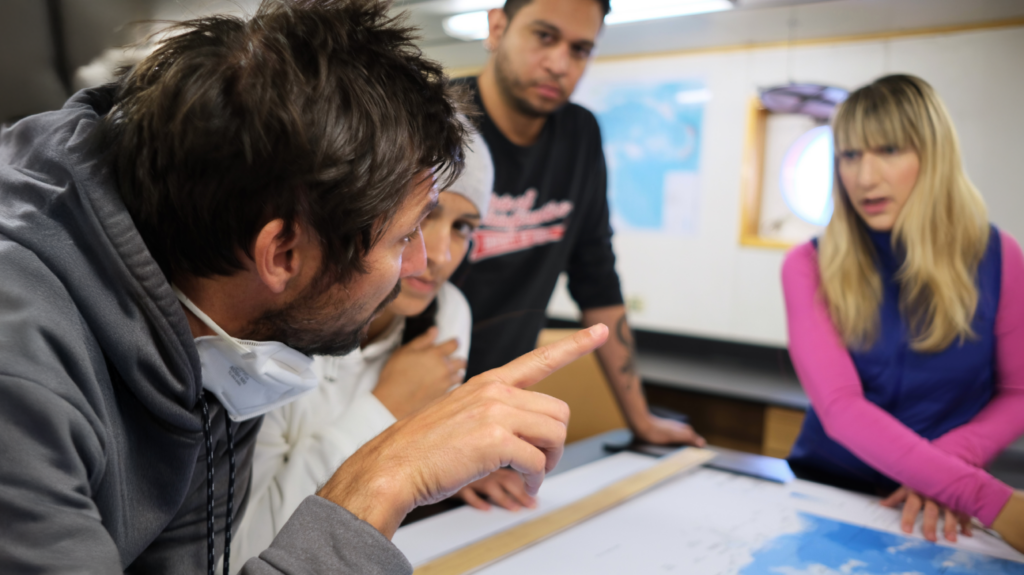 Holly Bik and her research team discuss at a table. Someone talks with his hands while the rest look at him. 