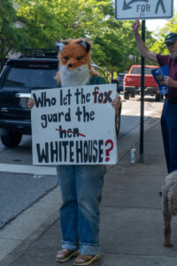A person wearing a fox mask holds a sign