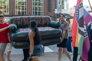 Two men walk holding a green inflatable couch spray painted with the word Fascists visable