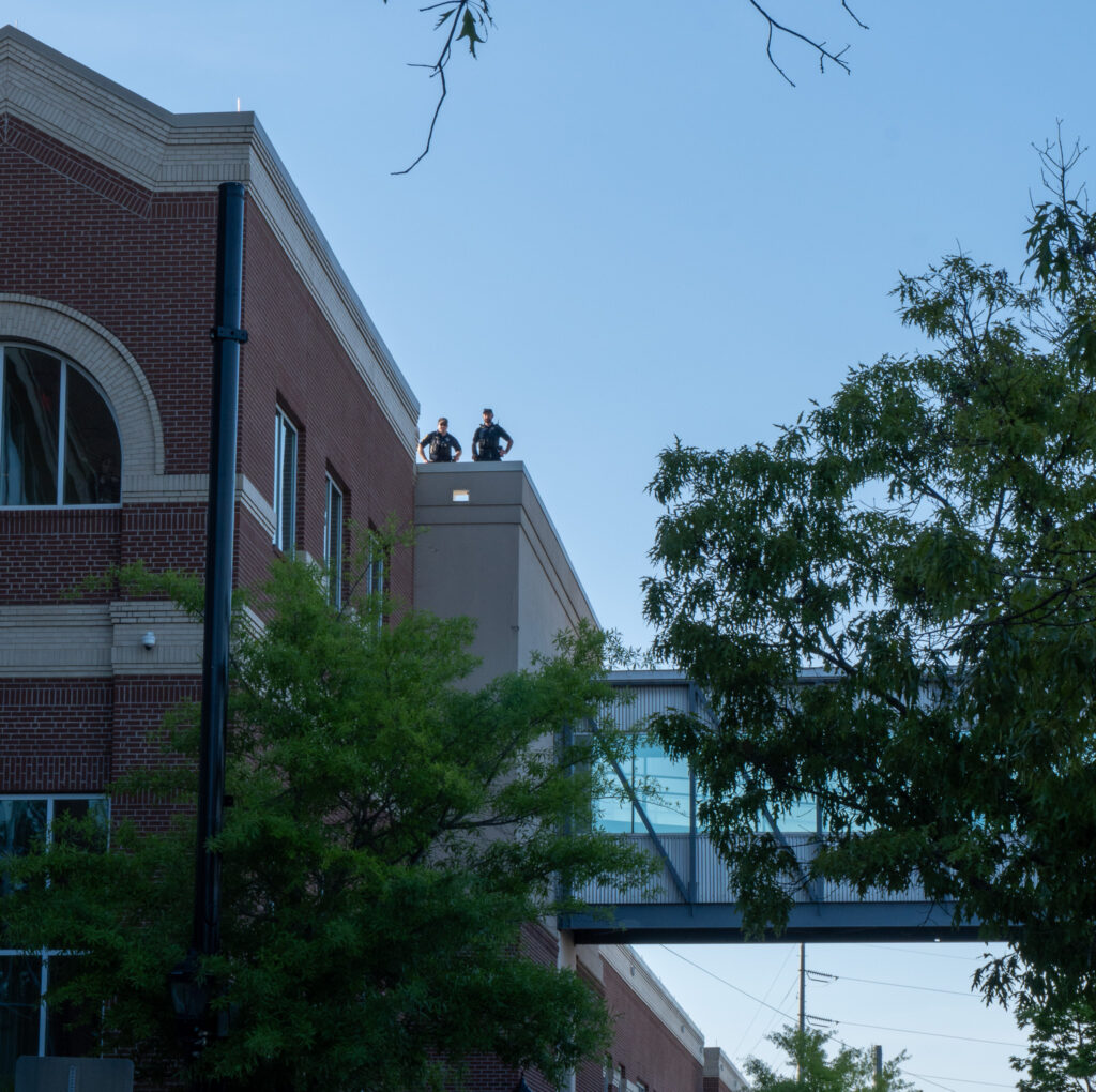 Two police officers on the roof a building watch over the protest