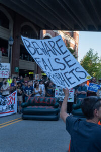 A woman holds a sign at the protest that reads "Beware False Prophets"