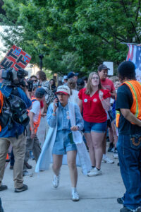 A woman in a hat that reads "Freedom" quickly walks towards camera with a phone in her hand.