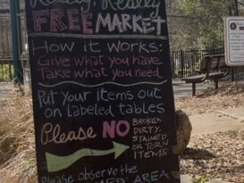 A sign reads: Really, Really Free Market. How it Works: Give what you have. Take what you need. Put your items out on Labeled tables. Please dirty, stained or torn items. Please observe the 'CLAIMED" area, items in this area are already claimed THIS IS A NO-MONEY MARKET. NO TRADE, SWAP, BARTER OR SALE