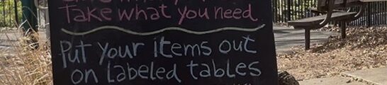 A sign reads: Really, Really Free Market. How it Works: Give what you have. Take what you need. Put your items out on Labeled tables. Please dirty, stained or torn items. Please observe the 'CLAIMED" area, items in this area are already claimed THIS IS A NO-MONEY MARKET. NO TRADE, SWAP, BARTER OR SALE