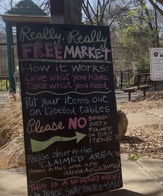 A sign reads: Really, Really Free Market. How it Works: Give what you have. Take what you need. Put your items out on Labeled tables. Please dirty, stained or torn items. Please observe the 'CLAIMED" area, items in this area are already claimed THIS IS A NO-MONEY MARKET. NO TRADE, SWAP, BARTER OR SALE