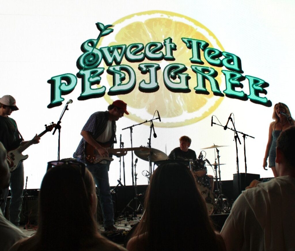 Sweet Tea Pedigree's logo, featuring their signature lemon slice, is projected behind them on a Jumbotron onstage.