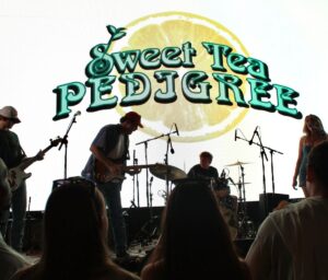Sweet Tea Pedigree's logo, featuring their signature lemon slice, is projected behind them on a Jumbotron onstage.