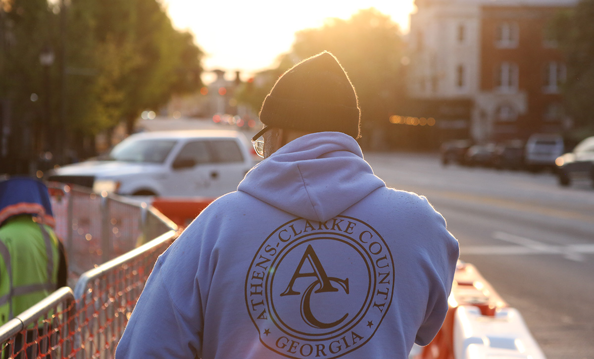 A man wearing a hoody walks to a truck next to a construction site. The sun is rising in the sky.